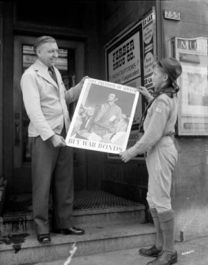 A Boy Scout helps display a poster promoting the purchase of war bonds in this 1943 photograph.