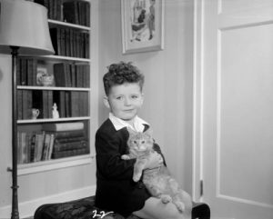 Photograph of a young boy in his home holding a cat, taken in 1948. 