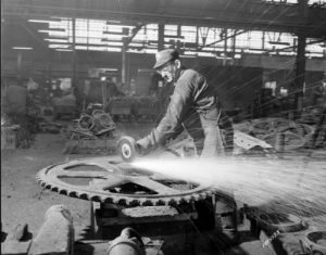 Photograph of a man grinding a large steel part at Pelton Steel Casting Company in 1956. 