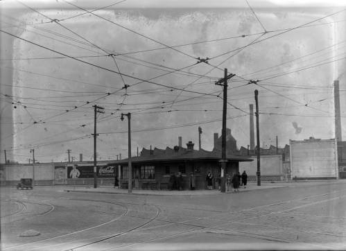 People wait for a streetcar in this 1932 photograph showing a station, the tracks embedded in the street, and the electrical network overhead.