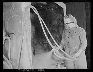 A woman sprays small parts for gasoline tanker trucks produced by the Heil Company in 1943 for the war effort.