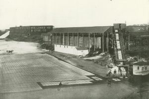 1906 illustration of men cutting ice blocks and loading it onto a conveyor belt at the right. 