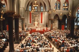 Photograph of a gathered congregation standing for mass held at Church of the Gesu. 