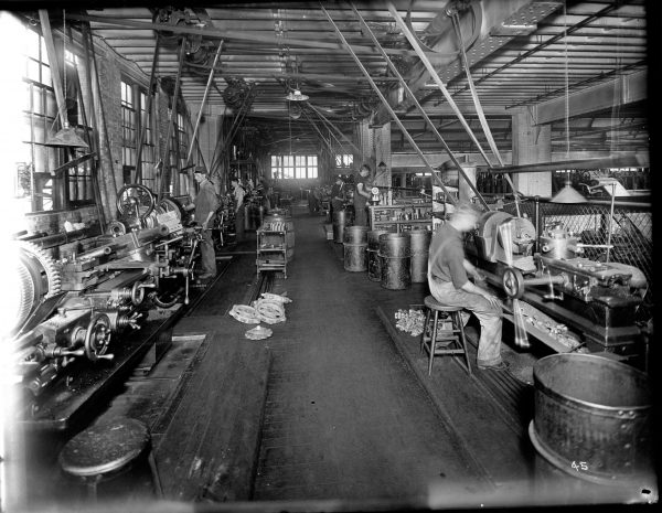 Chain Belt Company employees work at metal lathes. Finished parts and gears are stacked behind the men. 