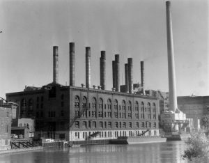 This undated photograph of the Wisconsin Electric Power plant shows coal barges transporting fuel on the Milwaukee River.