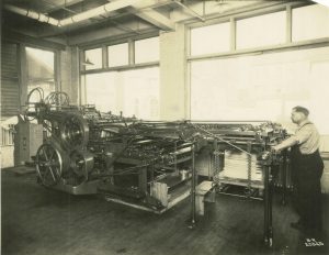 A man operates a long printing machine for the Krueger Printing Company. 