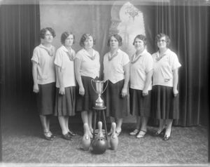 Group photograph of a women's bowling team standing behind a trophy in 1928.